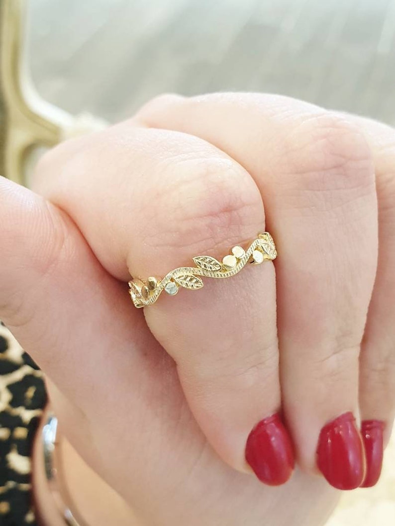 May include: A delicate gold ring with a leaf and flower design. The ring is on a finger with red nail polish.
