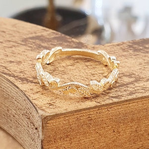 May include: A delicate gold ring with a leaf design. The ring is made of a thin band of metal and features a series of small leaves that are connected together.