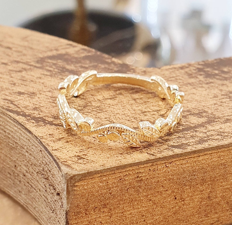 May include: A delicate gold ring with a leaf design. The ring is made of a thin band of metal and features a series of small leaves that are connected together.
