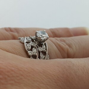 May include: A silver ring set with a large, round, clear diamond. The ring features a delicate, leafy design with smaller diamonds set around the main stone.
