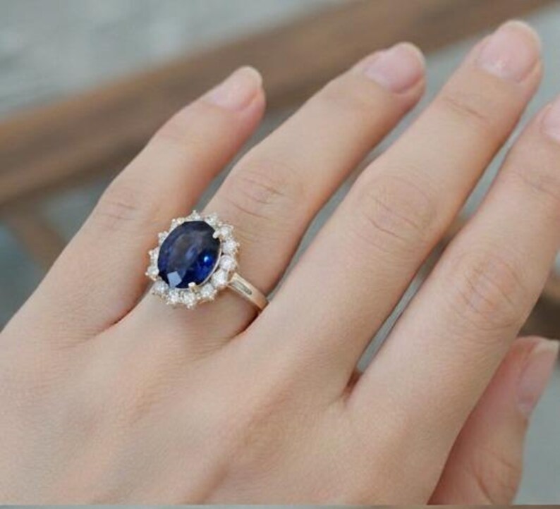 May include: A gold ring featuring a large, oval-cut, deep blue gemstone surrounded by a halo of smaller, clear gemstones. The ring is set on a delicate gold band, showcasing a classic and elegant design.