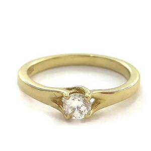 May include: A gold band ring with a single round clear stone set in the center.