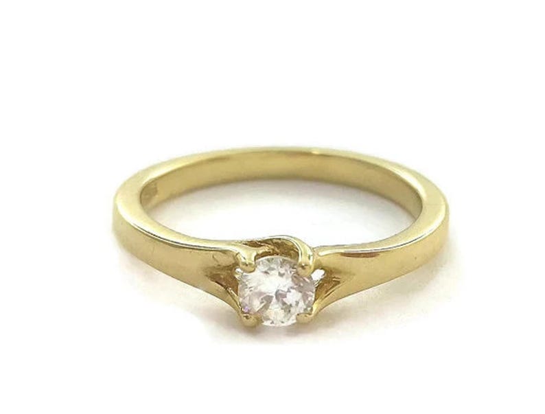 May include: A gold band ring with a single round clear stone set in the center.