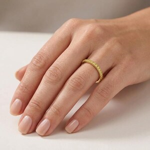 May include: A gold ring with a band of small, yellow gemstones. The ring is worn on a finger, showcasing its bright, polished appearance. The ring's design is simple yet elegant, with the gemstones set closely together.