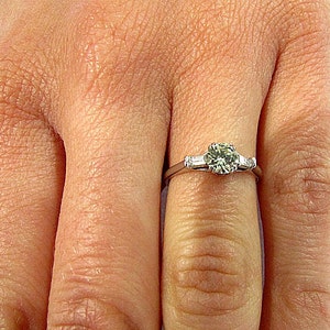 May include: A silver engagement ring with a round center diamond and two smaller diamonds on either side.