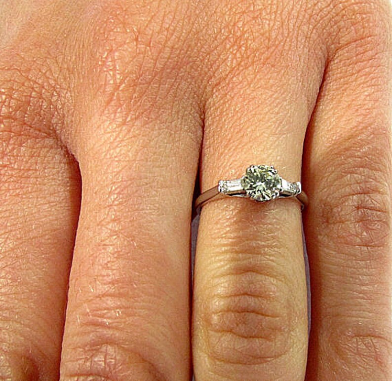 May include: A silver engagement ring with a round center diamond and two smaller diamonds on either side.