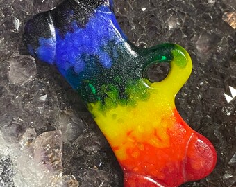 May include: A rainbow-colored resin bone charm with a black, blue, green, yellow, orange, and red color scheme. The charm has a hole at the top for attaching to a necklace or bracelet.