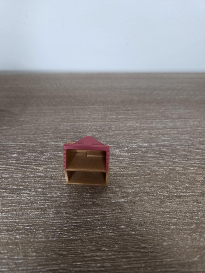 Pode incluir: Uma unidade de prateleira de madeira em miniatura com duas prateleiras e um telhado inclinado. A unidade &eacute; pintada em uma combina&ccedil;&atilde;o de marrom e uma cor rosa-avermelhada suave. As prateleiras est&atilde;o vazias.