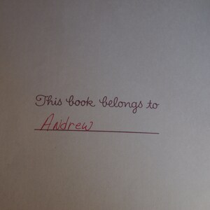 May include: A white book with the inscription "This book belongs to" followed by a line for a name. The name "Andrew" is written in red ink.