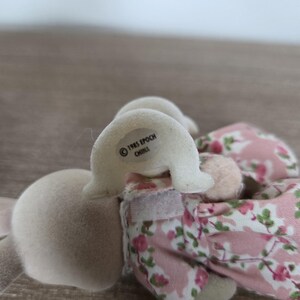 Pode incluir: Um coelho de brinquedo vintage com corpo rosa claro e orelhas brancas. O coelho usa um vestido floral rosa. O texto "1985 EPOCH CHINA" est&aacute; impresso na cabe&ccedil;a do coelho. O brinquedo &eacute; feito de material macio e felpudo.