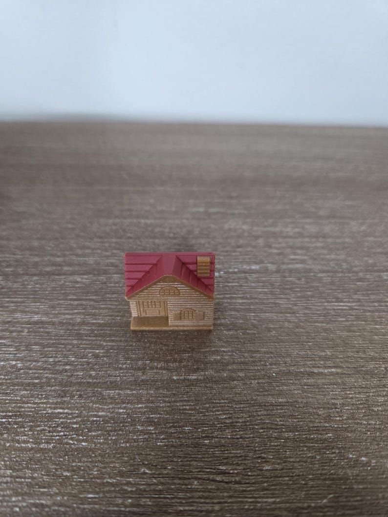 Pode incluir: Uma figura de casa em miniatura com telhado vermelho, paredes bege e uma pequena chamin&eacute;. A casa tem uma porta da frente e janelas. A figura est&aacute; sobre um fundo de madeira.