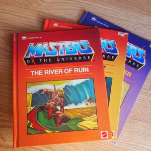 May include: Three paperback books with orange, yellow and purple covers. The covers feature the Masters of the Universe logo and the title "The River of Ruin".