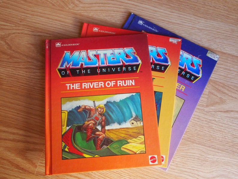 May include: Three paperback books with orange, yellow and purple covers. The covers feature the Masters of the Universe logo and the title "The River of Ruin".