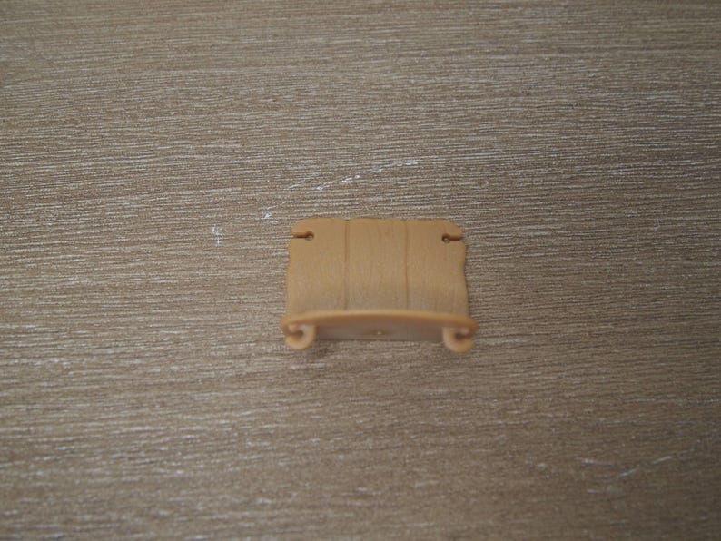 May include: A small, tan-colored decorative shelf with a scroll design on the ends. The shelf has a flat surface and two small holes at the top for hanging. The shelf is made of a smooth material.