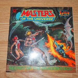 May include: A vintage Masters of the Universe comic book cover featuring He-Man, Teela, and a dragon. The cover is titled "Secret of the Dragon's Egg" and features a golden "Super Adventure Book" logo.