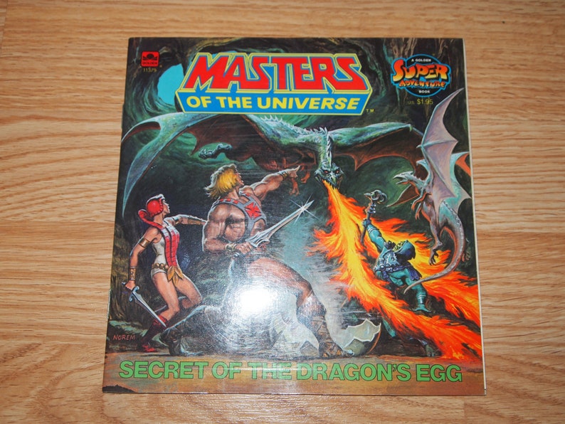May include: A vintage Masters of the Universe comic book cover featuring He-Man, Teela, and a dragon. The cover is titled "Secret of the Dragon's Egg" and features a golden "Super Adventure Book" logo.