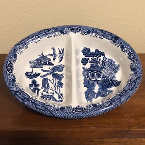May include: A divided serving dish with a blue and white willow pattern. The dish is oval shaped and has a white background with blue floral and landscape designs.
