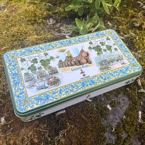 May include: A rectangular tin with a decorative lid featuring a winery scene with the text "Gonzalez Byass" and "Tio Pepe." The tin has a blue and white floral border and a green trim.