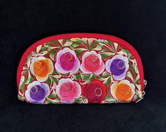 May include: A red, semi-circular embroidered clutch with a zipper closure. The clutch features a floral design with colorful flowers in shades of pink, orange, purple, and red, set against a green and red background.