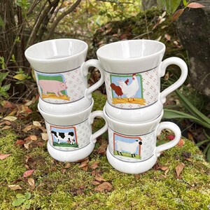 May include: Four white ceramic mugs stacked on top of each other. Each mug features a different farm animal illustration: a pig, a cow, a chicken, and a sheep. The mugs have a handle and a decorative pattern.