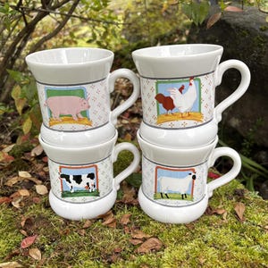 May include: Four white ceramic mugs stacked, each with a different farm animal illustration: a pig, a chicken, a cow, and a sheep. The mugs have a patterned border and a curved handle. The mugs are on a mossy surface.