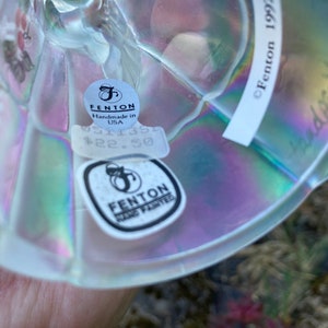 May include: A clear glass iridescent Fenton hand-painted figurine with a sticker that reads "Fenton Handmade in USA 0511354 $22.50" and another sticker that reads "Fenton Hand Painted" and the text "&copy; Fenton 1992".