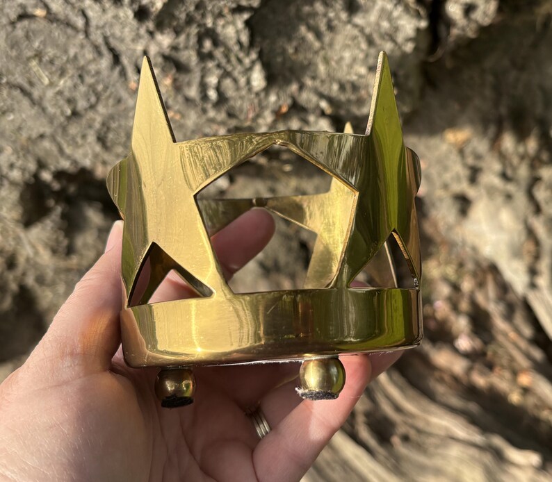 Puede incluir: Un portavelas de metal dorado con recortes de estrellas. El portavelas tiene forma cil&iacute;ndrica con tres peque&ntilde;os pies de bola. Los recortes de estrellas est&aacute;n espaciados uniformemente alrededor de la circunferencia.