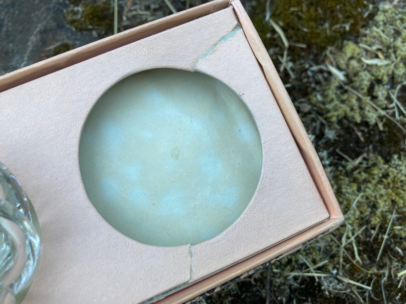 May include: A close-up of a light pink cardboard box with a circular cutout. The cutout is for a round object, such as a candle or a soap.