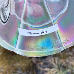 May include: A clear glass iridescent Fenton paperweight with a label that reads "Fenton 1992" and a handwritten signature that reads "handpainted by Nelson".