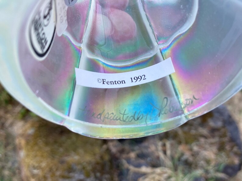 May include: A clear glass iridescent Fenton paperweight with a label that reads "Fenton 1992" and a handwritten signature that reads "handpainted by Nelson".