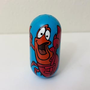 May include: A blue, oval-shaped toy featuring a cartoon crab character with a red body and claws, and a smiling face. The crab is set against a bright blue background.