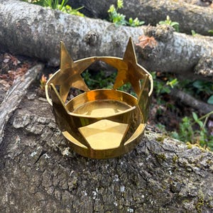 Puede incluir: Un portavelas de metal dorado con recortes de estrellas y una base circular. El portavelas est&aacute; dise&ntilde;ado para sostener una vela peque&ntilde;a y tiene un dise&ntilde;o decorativo de estrellas en la parte superior.