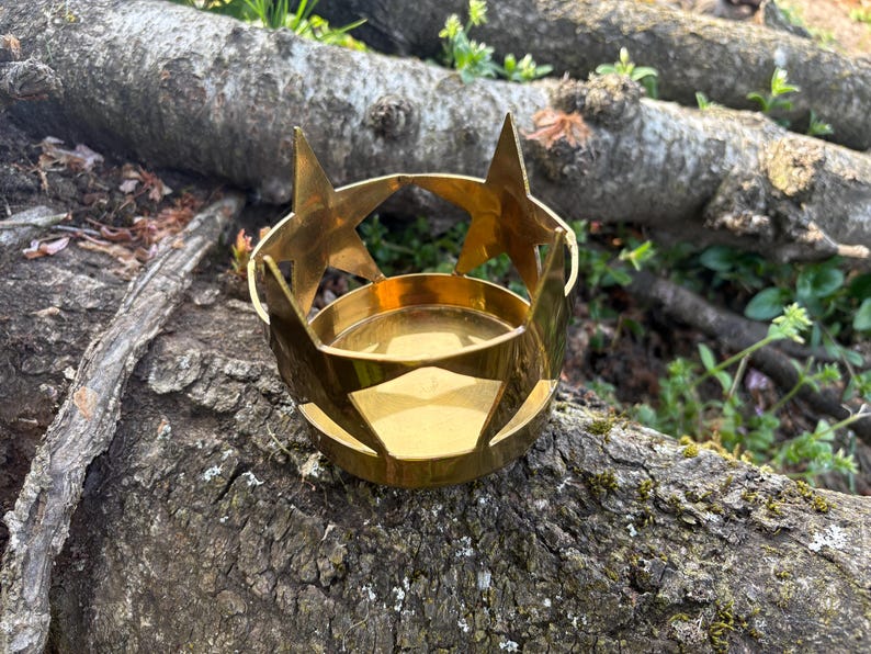 Puede incluir: Un portavelas de metal dorado con recortes de estrellas y una base circular. El portavelas est&aacute; dise&ntilde;ado para sostener una vela peque&ntilde;a y tiene un dise&ntilde;o decorativo de estrellas en la parte superior.
