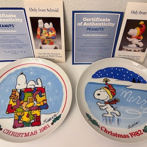 May include: Two round ceramic collector plates featuring Peanuts characters. The 1981 plate shows Snoopy on a doghouse with colorful stockings. The 1982 plate depicts Snoopy ice skating with the text Merry. Both include certificates of authenticity.