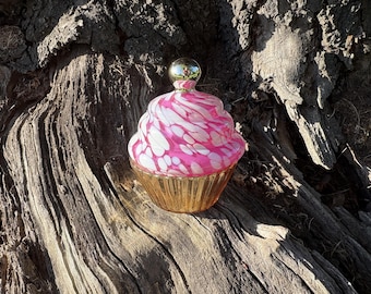 Vela perfumada em formato de cupcake, com aroma de framboesa e rosa, em frasco de vidro com detalhes dourados e rosa.