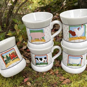 May include: White ceramic mugs with farm animal illustrations. Each mug features a different animal: a pig, a cow, a chicken, and a sheep. The mugs have a handle and a decorative border with a farm scene.
