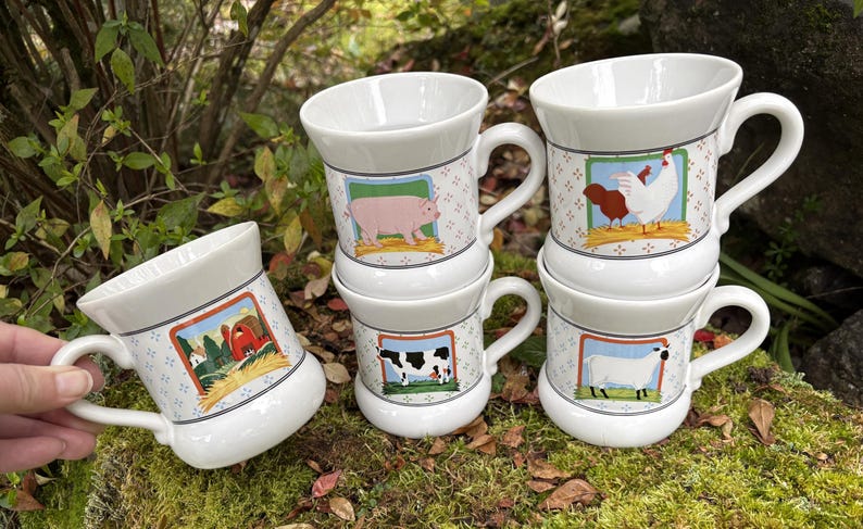May include: White ceramic mugs with farm animal illustrations. Each mug features a different animal: a pig, a cow, a chicken, and a sheep. The mugs have a handle and a decorative border with a farm scene.