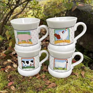 May include: Four white ceramic mugs stacked, each with a different farm animal illustration: a pig, a rooster and hen, a cow, and a sheep. The mugs have a patterned design and are set on a bed of moss.
