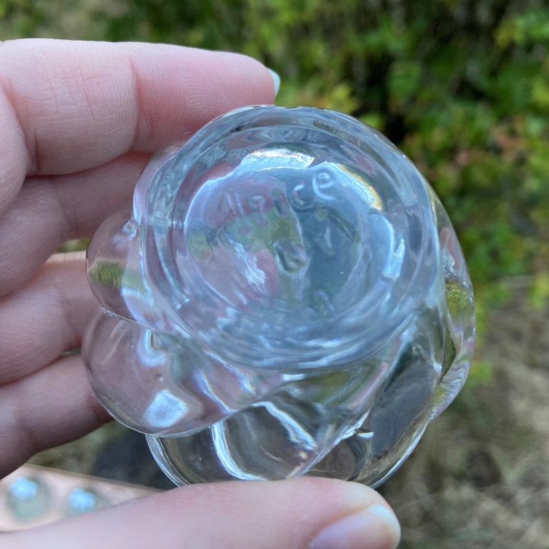May include: Clear glass bud vase with a wavy, textured design. The bottom of the vase is marked with the text "Alice 12".