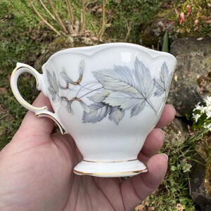 May include: A set of three ceramic mugs with a speckled, matte finish. The mugs are in shades of cream, light gray, and dark gray. Each mug has a simple, minimalist design and a rounded handle.