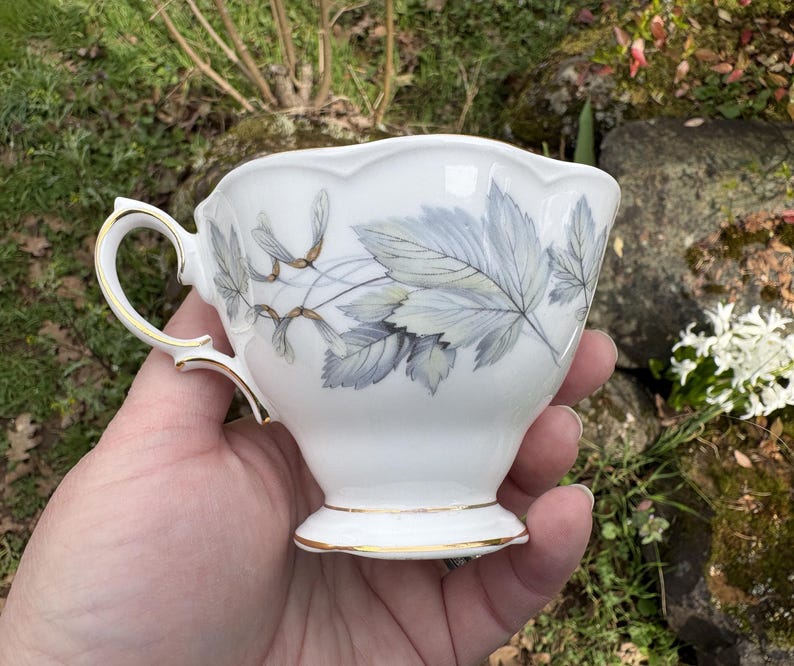 May include: A set of three ceramic mugs with a speckled, matte finish. The mugs are in shades of cream, light gray, and dark gray. Each mug has a simple, minimalist design and a rounded handle.