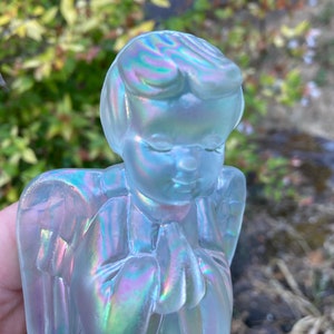 May include: A glass angel figurine with iridescent wings and a praying pose. The angel is made of clear glass with a pearlescent finish.