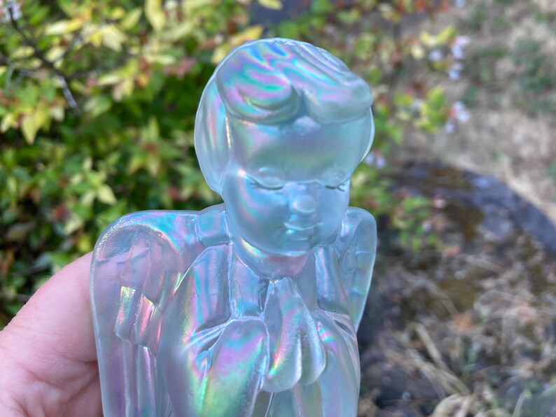 May include: A glass angel figurine with iridescent wings and a praying pose. The angel is made of clear glass with a pearlescent finish.