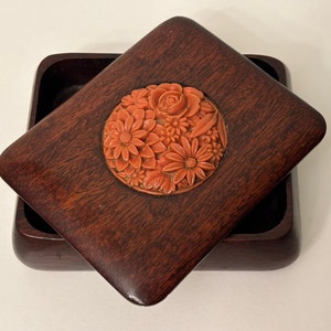 May include: A wooden box with a hinged lid. The lid features a carved floral design in a bright orange color.