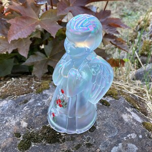 May include: A white iridescent glass angel figurine with painted red berries and white flowers. The angel is standing with its hands clasped in prayer and has wings.
