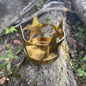 Puede incluir: Un portavelas de lat&oacute;n con dise&ntilde;o de estrella. El soporte tiene una base circular y est&aacute; adornado con estrellas recortadas. El lat&oacute;n tiene un tono dorado c&aacute;lido y el dise&ntilde;o es simple pero elegante. El portavelas se utiliza probablemente con fines decorativos.