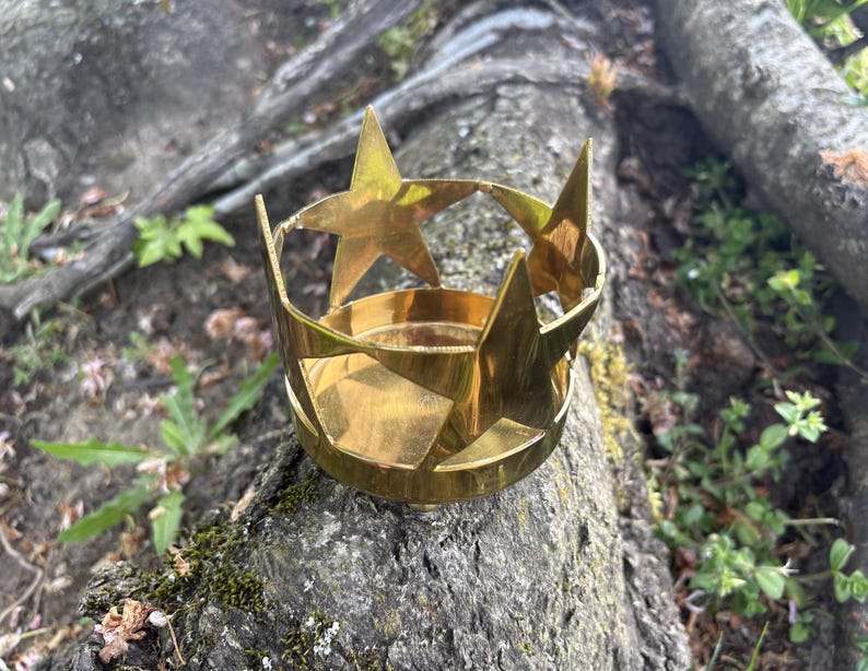 Puede incluir: Un portavelas de lat&oacute;n con dise&ntilde;o de estrella. El soporte tiene una base circular y est&aacute; adornado con estrellas recortadas. El lat&oacute;n tiene un tono dorado c&aacute;lido y el dise&ntilde;o es simple pero elegante. El portavelas se utiliza probablemente con fines decorativos.