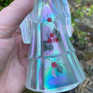 May include: A clear iridescent glass angel figurine with hand-painted red berries and green leaves on its dress.