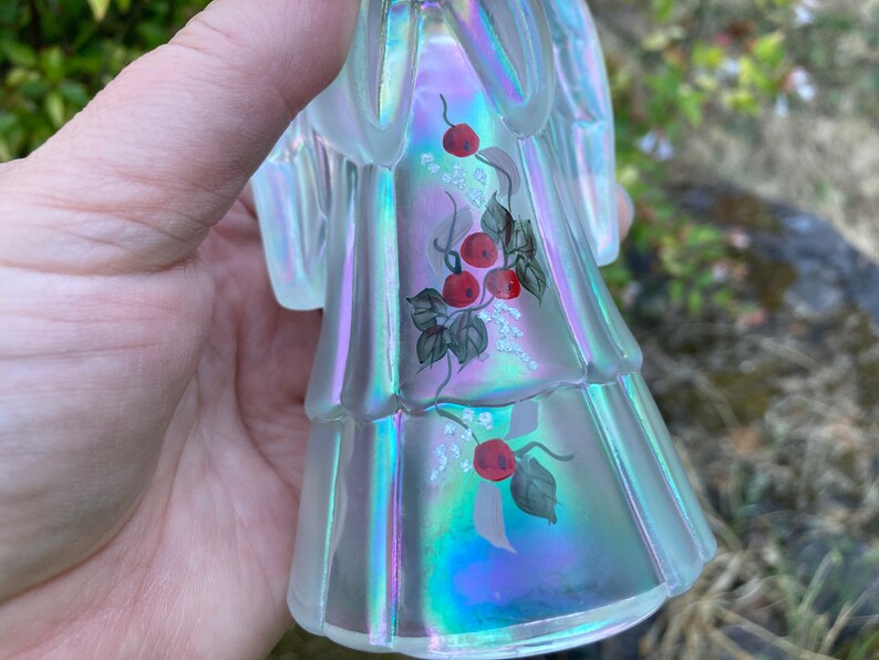 May include: A clear iridescent glass angel figurine with hand-painted red berries and green leaves on its dress.