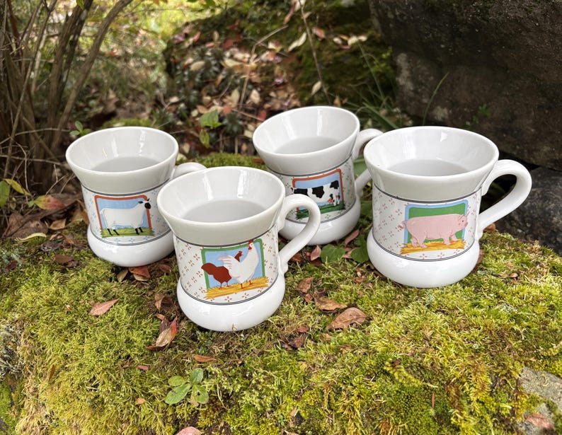 May include: Four white ceramic mugs with farm animal illustrations. Each mug features a different animal: a sheep, a cow, a pig, and a chicken. The mugs have a handle and a decorative border with a patterned design.
